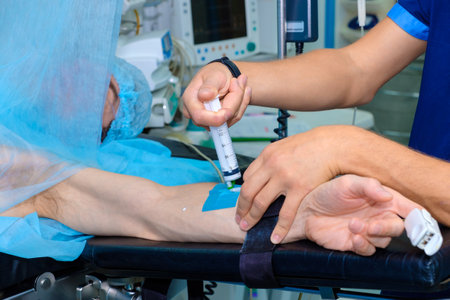 An anesthesiologist injects intravenous anesthesia with a large syringe into the patient's arm on the operating table. Surgery with general anesthesia.の写真素材