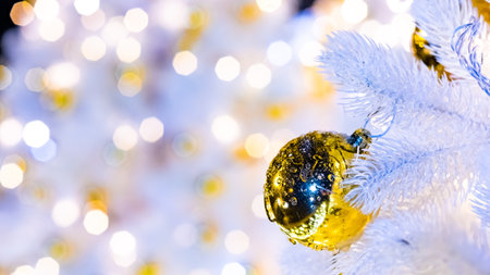 Ice-covered Christmas ball on white fir branches with golden Christmas lights on an abstract defocused background. Selective focus. Decoration on the New Year's tree.の写真素材