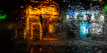 Blurred lights of the night city through drops on the glass. Selective focus on water drops on glass. Abstract background.の写真素材