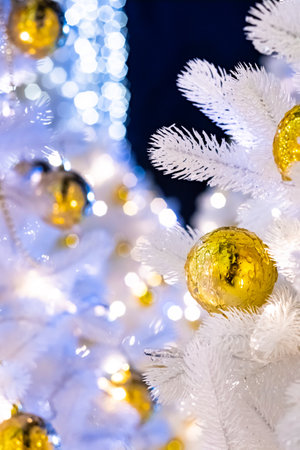 Selective focus on golden iced Christmas ball on white artificial fir branches. Defocused background with New Year decorations and lights.の写真素材