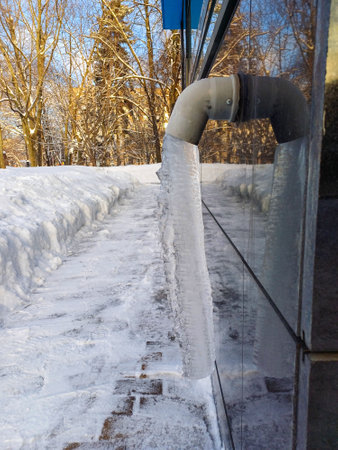 Drainpipe with frozen stream of water outdoors on a sunny frosty winter day.の写真素材