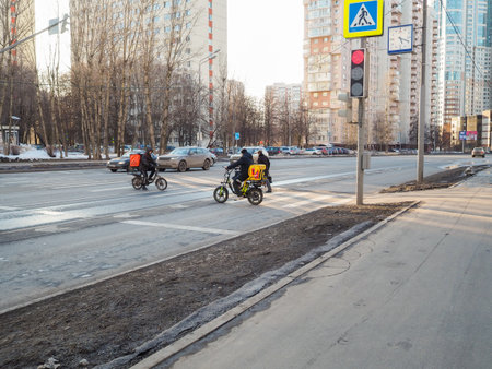 Couriers on electric bicycles at a pedestrian crossing in the city. Moscow. Russia. March 21, 2024.のeditorial素材