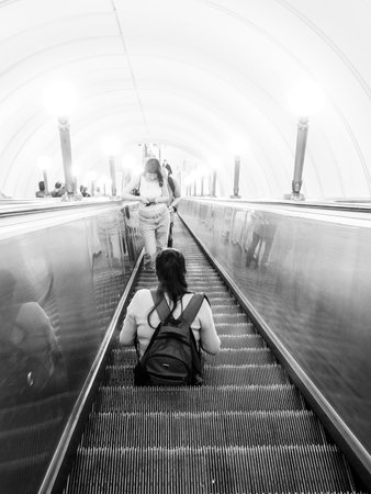Rear view of a woman sitting on the steps of a subway escalator. Black and white photo. Selective focus. Moscow. Russia. June 19, 2024.のeditorial素材