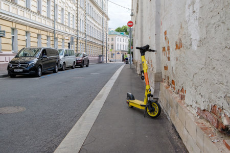 A lonely yellow rental scooter, owned by the Yandex company, stands on the sidewalk of a city street on a summer day. Moscow. Russia. June 30, 2024.のeditorial素材