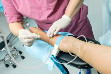 The doctor in sterile gloves wipes the patients hand with an alcohol solution before installing the dropper catheter.の写真素材