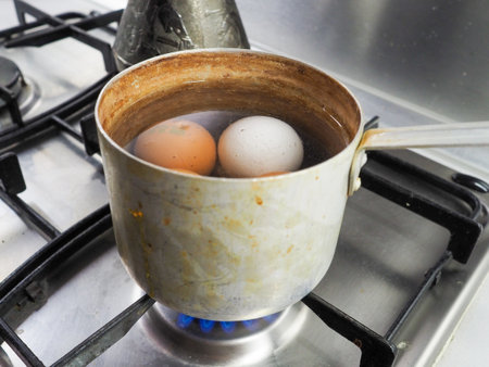 Chicken eggs are boiled in a dirty aluminum pan on a gas stove.の写真素材