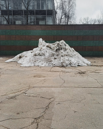 A large dirty pile of snow on dry cracked asphalt.