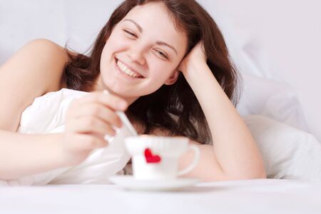 happy woman in bed and cup with heart in front of herの写真素材