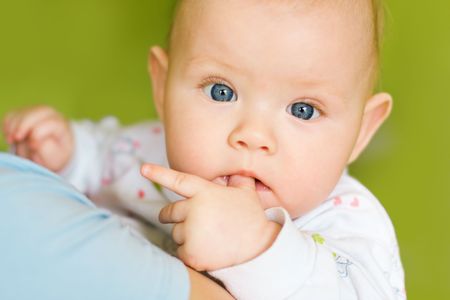 portrait of baby with finger in mouth on green background