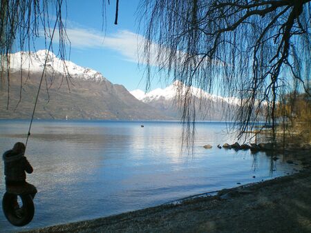 Silhouette of a child on a tyre swing, with a lake and mountainsの写真素材
