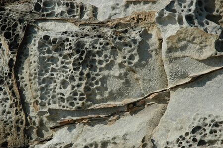 Close-up of eroded rocks at the beach. The rocks show cracks and weathering. They are grey with rust coloured markings.の写真素材