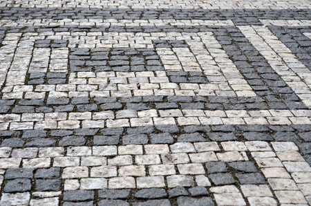 Black and grey cobblestones of a footpath have been laid in a geometrical pattern. They are worn with time.の写真素材