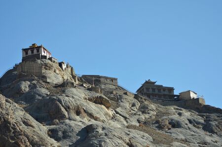 White monastery buildings are seen against a clear blue sky in Ladakh, India. Prayer flags are hung along a path on top of the rocky hill leading to the Buddhist monastery.の写真素材
