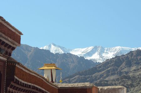 A small tower with a golden roof sits on top of the roof of a Buddhist monastery in Ladakh, India. Behind are mountains leading to the snow-capped Ladakh Range, part of the Tibet Himalayan Region.の写真素材