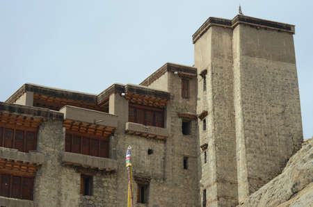 Details of the grey stone and wooden doors and windows of Leh Palace in Ladakh, India. There is a tower at the far end. A prayer flag is in the foreground, and the sky is blue.のeditorial素材