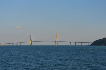 A bridge arches over a bay from an island  to the mainland. Two pylons, with radiating supportive metal struts, rise above the bridge to form an architectural feature. The sky is blue with clouds.の写真素材