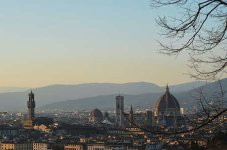 The bare branches of a tree frame the view over the city of Florence, Italy at dusk. The Duomo, Baptistery and Campanile dominate the skyline. Hills are in the background. The sky is clear.の写真素材