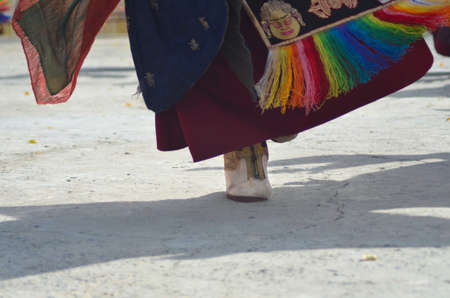 A monk is performing a dance in a Buddhist temple in Ladakh, India. Only his foot , shadow and the bottom of his robe are visible. His shoe is white leather with gold trim, while colourful fabrics adorn his red robe.の写真素材