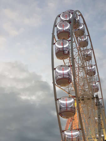 The cabins of a ferris-wheel have been lit up for evening. they are seen from below, against white...