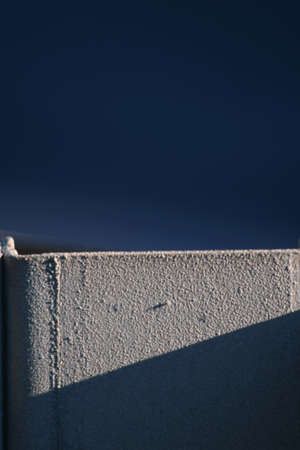 The texture of a concrete wall makes an abstract design against a dark blue background. A sharp shadow falls across the pale concrete.の写真素材