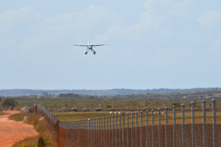 A fixed wing amphibious plane is landing over a field of scrub. A fence divides the landing field form a road of red dirt. The image of the plane is distorted by hot air.の写真素材