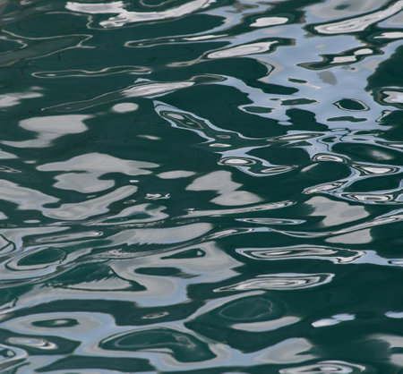 Sunlight is reflected off dark green water. The light is distorted by the movement of the water, creating an abstract image.の写真素材