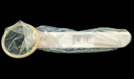 Safe sex or pregnancy concept. Positive pregnancy test in condom over blackの写真素材