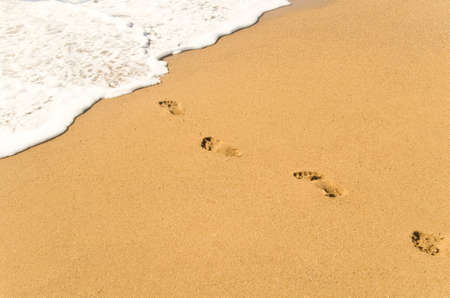 Footprints on sand ending in wave foamの写真素材