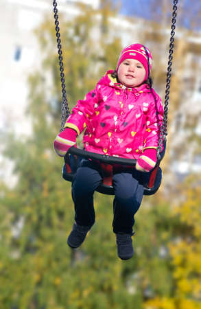 Little girl shaking on swing in sunny late autumnの写真素材