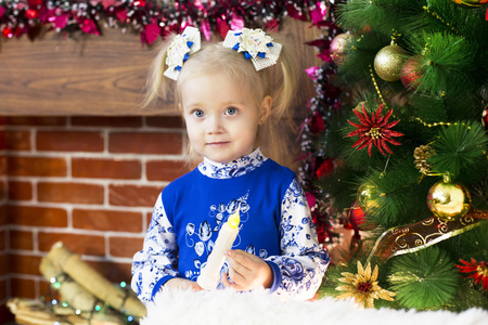 A funny young girl in a blue dress is having fun near the Christmas tree at home.の写真素材
