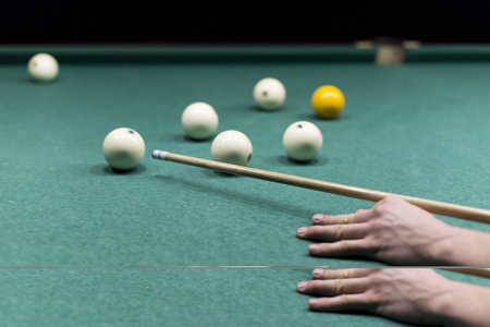 Billiards close-up on the green. Hands of a man holding a stick for playing billiards and aiming at...