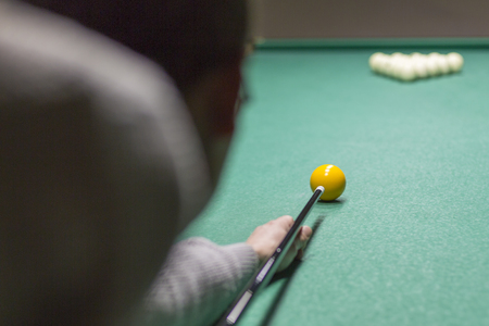 Billiards close-up on the green. Hands of a man holding a stick for playing billiards and aiming at...