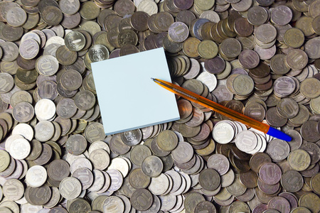 A pen and a block on coins. A bunch of metal coins on which a pencil and a writing paper.の写真素材