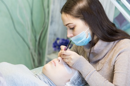 Volumetric eyelash extends in the beauty salon. The procedure for increasing eyelashes in front of a blonde girlの写真素材