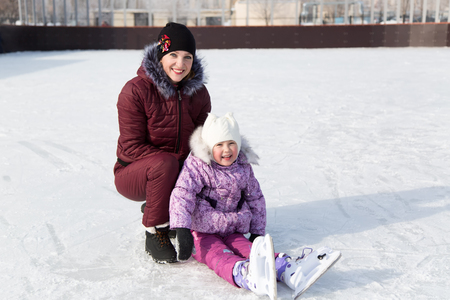Mom learns a daughter to skate. A young mother and little daughter embrace and kiss on a winter walk.の写真素材
