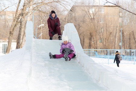 Mom and daughter are riding from a snowy mountain. A young mother and her little daughter are having fun outside in the winter.の写真素材