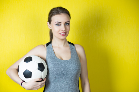 Girl with a soccer ball on a yellow background. A beautiful girl in a gray sports suit.の写真素材