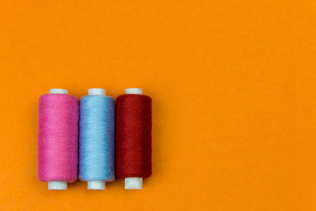 The coils with threads stand vertically on an orange background. A row of coils with bright colored...