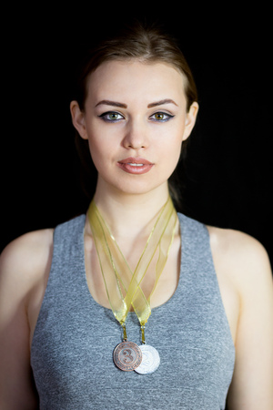 A beautiful sportswoman in a gray suit with a medal around her neck. Young winner of the competition with a reward for success in the sport on a black background.の写真素材