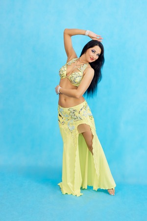 Charming dancer performs oriental belly dance on a blue background. A girl in a yellow dress is dancing an oriental belly dance on a blue background.の写真素材