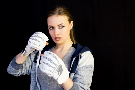 Girl sportswoman in gloves for boxing on a black background. The girl is a fighter of mixed martial arts who covers her face with gloves from blows.の写真素材