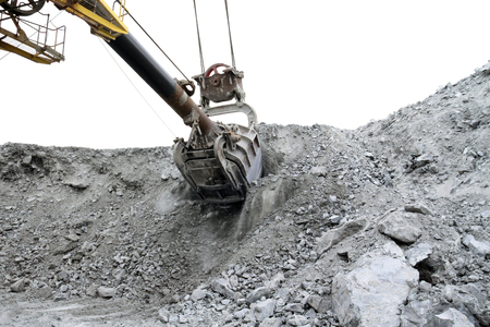 The excavator rakes a bunch of stones in the quarry. The bucket of the excavator cuts into a...