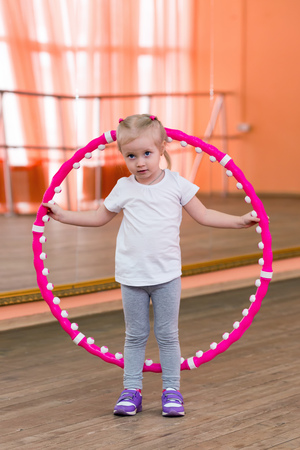 The little girl is 3 years old in the gym. A girl with white hair goes in for sports with a hoop.の写真素材