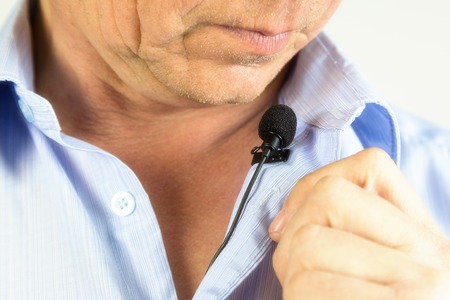 The man speaks into a small microphone in a low voice. The lips of a man in a lapel microphone.の写真素材