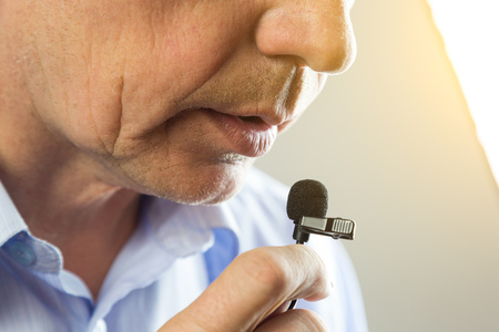 The man speaks into a small microphone in a low voice. The lips of a man in a lapel microphone.の写真素材
