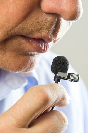 The man speaks into a small microphone in a low voice. The lips of a man in a lapel microphone.の写真素材