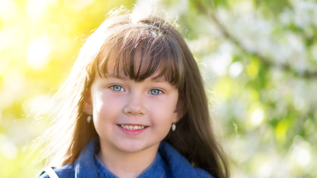 Portrait of a girl in blossoming apple tree. A little girl of 5 years of age in a jeans dress among the flowers in a spring apple orchard.の写真素材