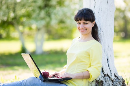 A girl is sitting with a laptop near a tree.の写真素材