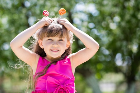 The girl is playing with big sweets on a stick. A child from sweets makes a horn.の写真素材