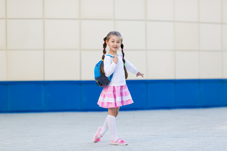 The girl is a young fashionista posing. A pretty girl in a summer dress with a backpack is standing by the wall in the city.の写真素材